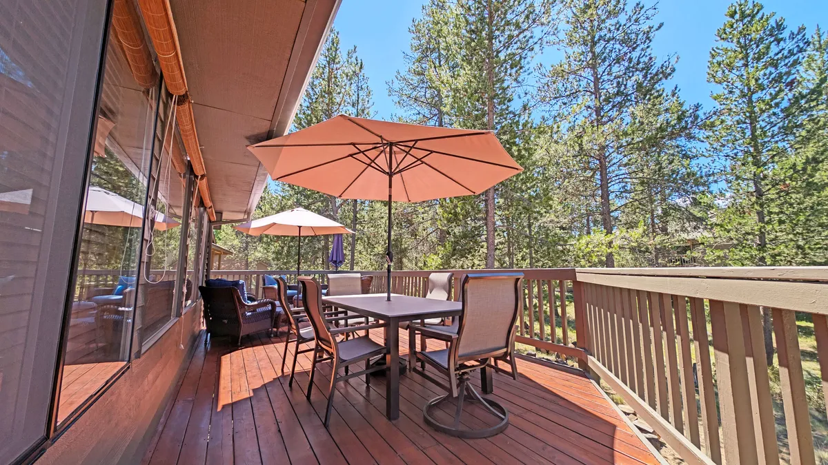 A cheerful outdoor dining scene with a large table, umbrellas for shade, and a backdrop of vibrant greenery. The setting is ideal for group meals, morning coffee, or sunset gatherings in a resort-like ambiance.