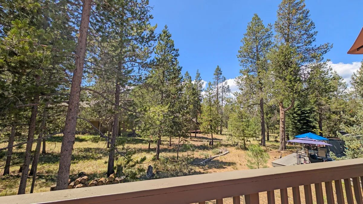 This exterior shot captures tall pine trees, a spacious open grassy area, and a patio with an umbrella, inviting guests to step outdoors. The environment hints at the natural beauty and peacefulness surrounding Red Cedar 53, with the patio serving as a comfortable base for relaxation or launching into outdoor activities.
