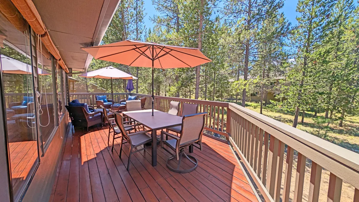 A serene outdoor dining area featuring tables with umbrellas and comfortable seating, nestled among mature trees. The space invites guests to relax, dine al fresco, or enjoy casual conversations in the fresh air.