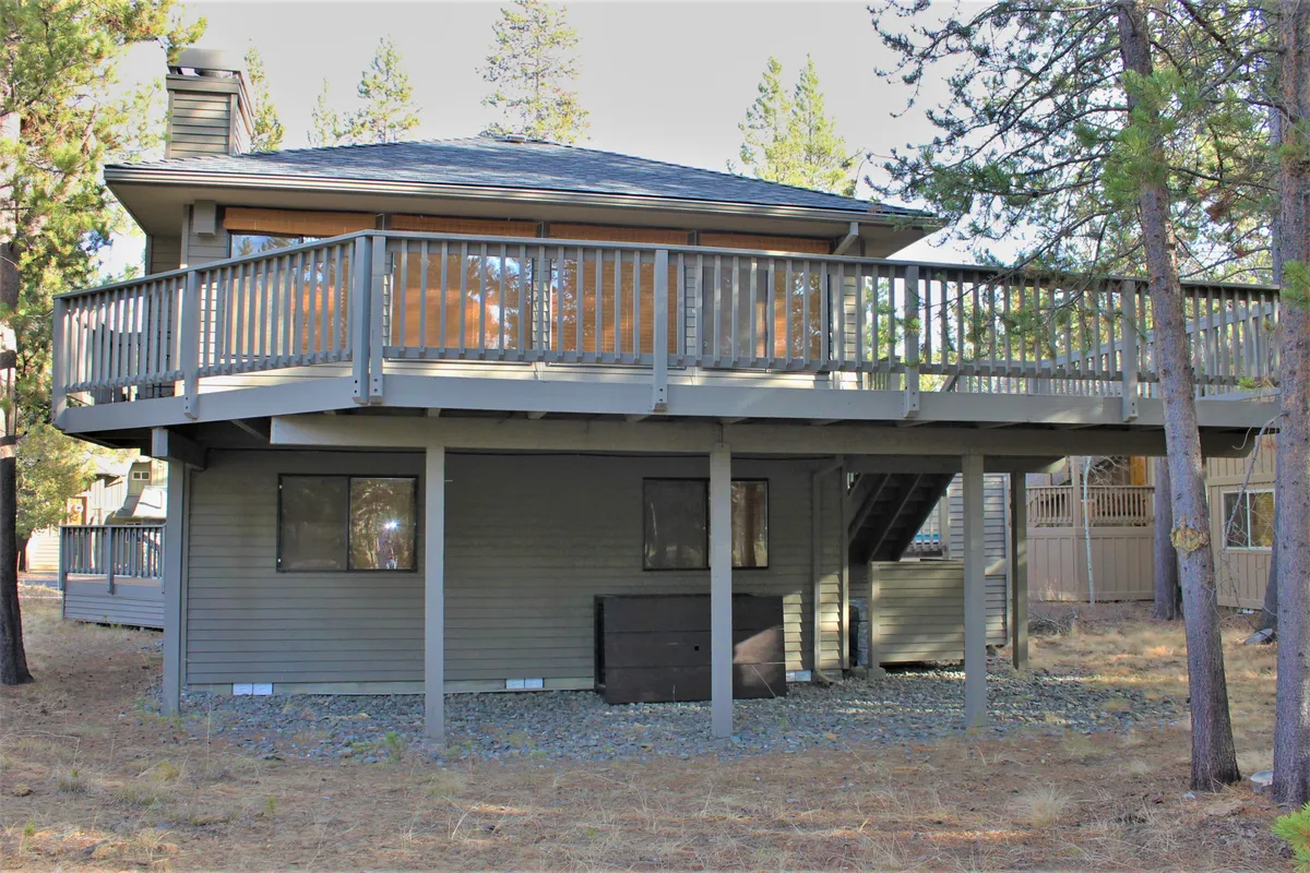 An inviting deck nestled among trees, with windows reflecting natural light and a sense of privacy. The scene suggests opportunities for outdoor dining, relaxation, or simply enjoying the wooded surroundings, which are integral to the Sunriver experience.