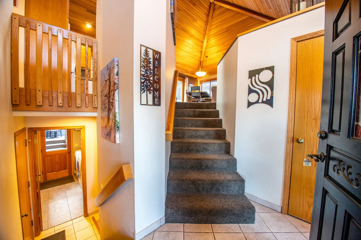 A view of the staircase leading upstairs to the main living and kitchen area, accented by a 'WELCOME' sign and warm wooden details. The image sets the stage for arriving at the heart of the home and hints at the journey toward shared spaces.