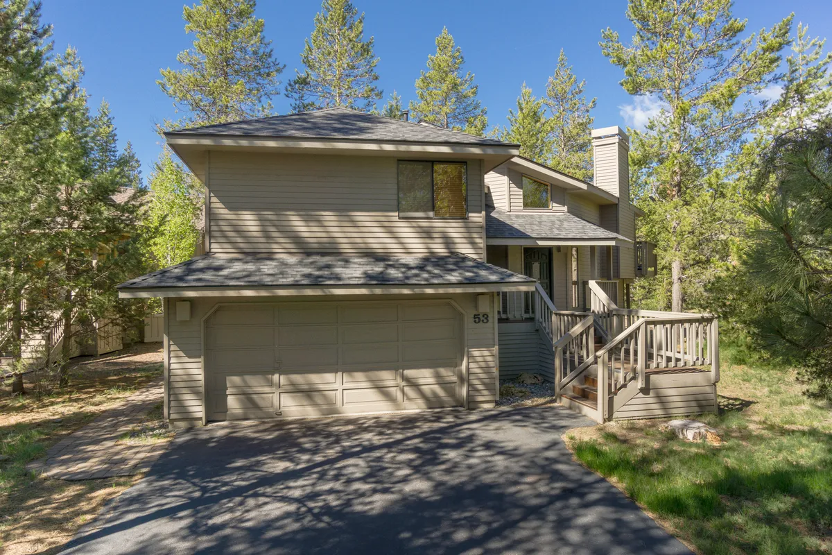 A wide view of the exterior shows the home’s two-story architecture and expansive deck set amongst tall pine trees. The scene evokes a welcoming atmosphere, ideal for family gatherings, BBQs, or simply enjoying the outdoors before or after exploring Sunriver’s attractions.