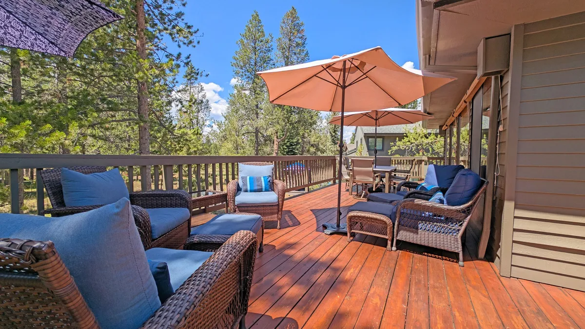 A beautiful wooden deck set against lush natural surroundings, featuring comfortable wicker chairs, large umbrellas for shade, and plenty of space for social gatherings or morning coffee. The environment is tranquil yet vibrant.
