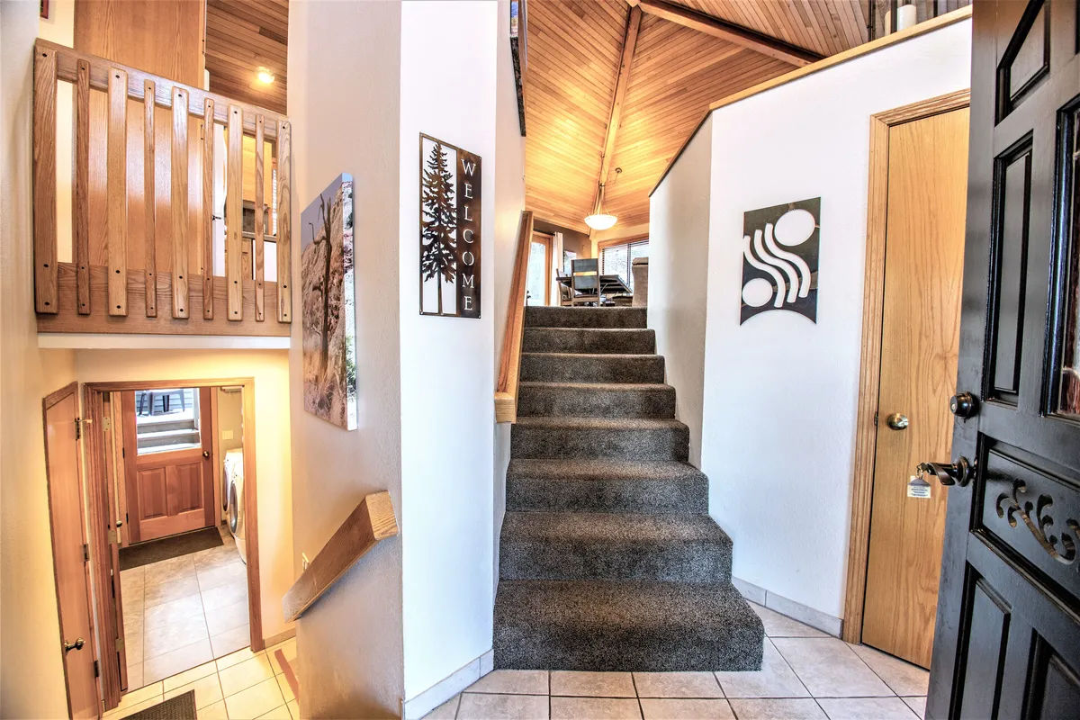 The entryway features a staircase with a wooden railing, a welcoming sign, and wall art, providing a warm and inviting introduction to the home. The scene bridges the transition from outdoor adventures to the comfort and hospitality inside Red Cedar 53.